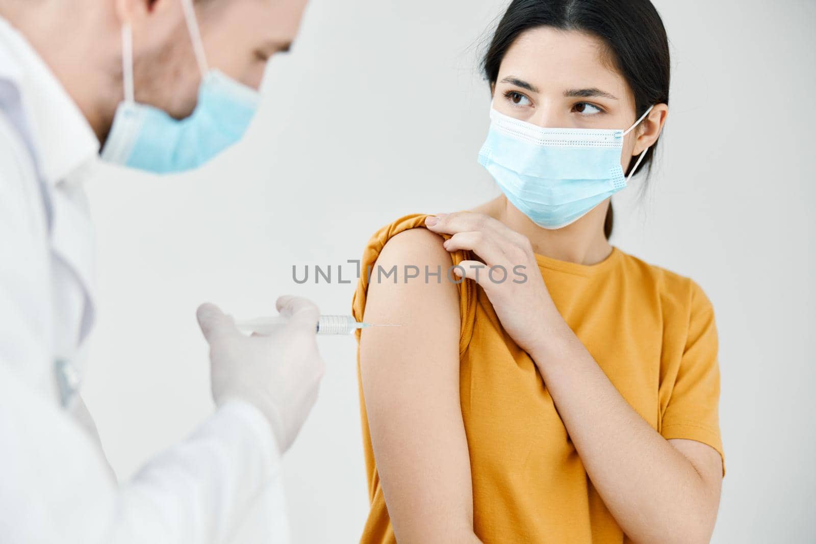a professional doctor in a white coat injects a vaccine into the shoulder of a woman in a medical mask vaccination by SHOTPRIME