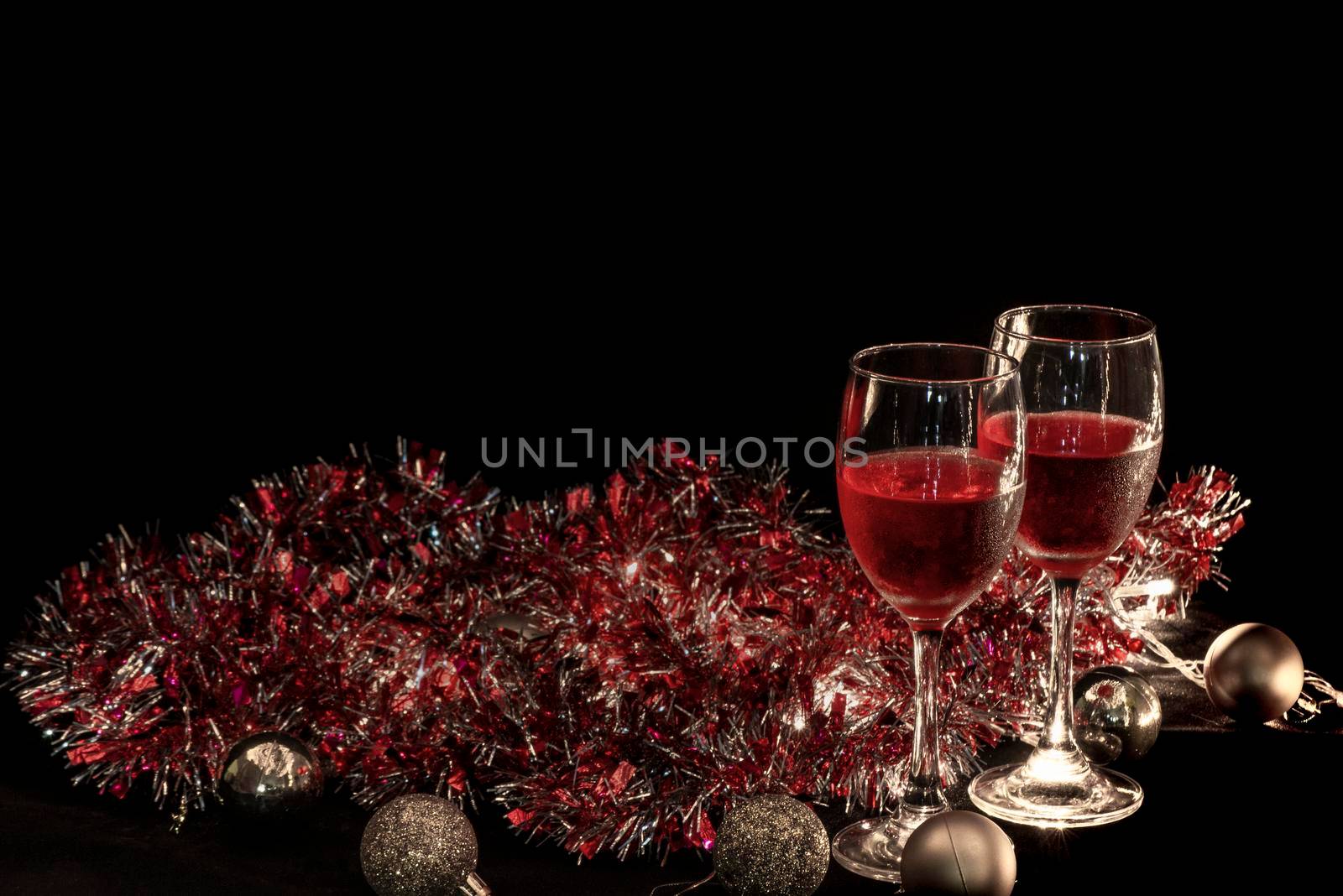 christmas atmosphere,two red wine glass against christmas lights decoration background. by thanumporn