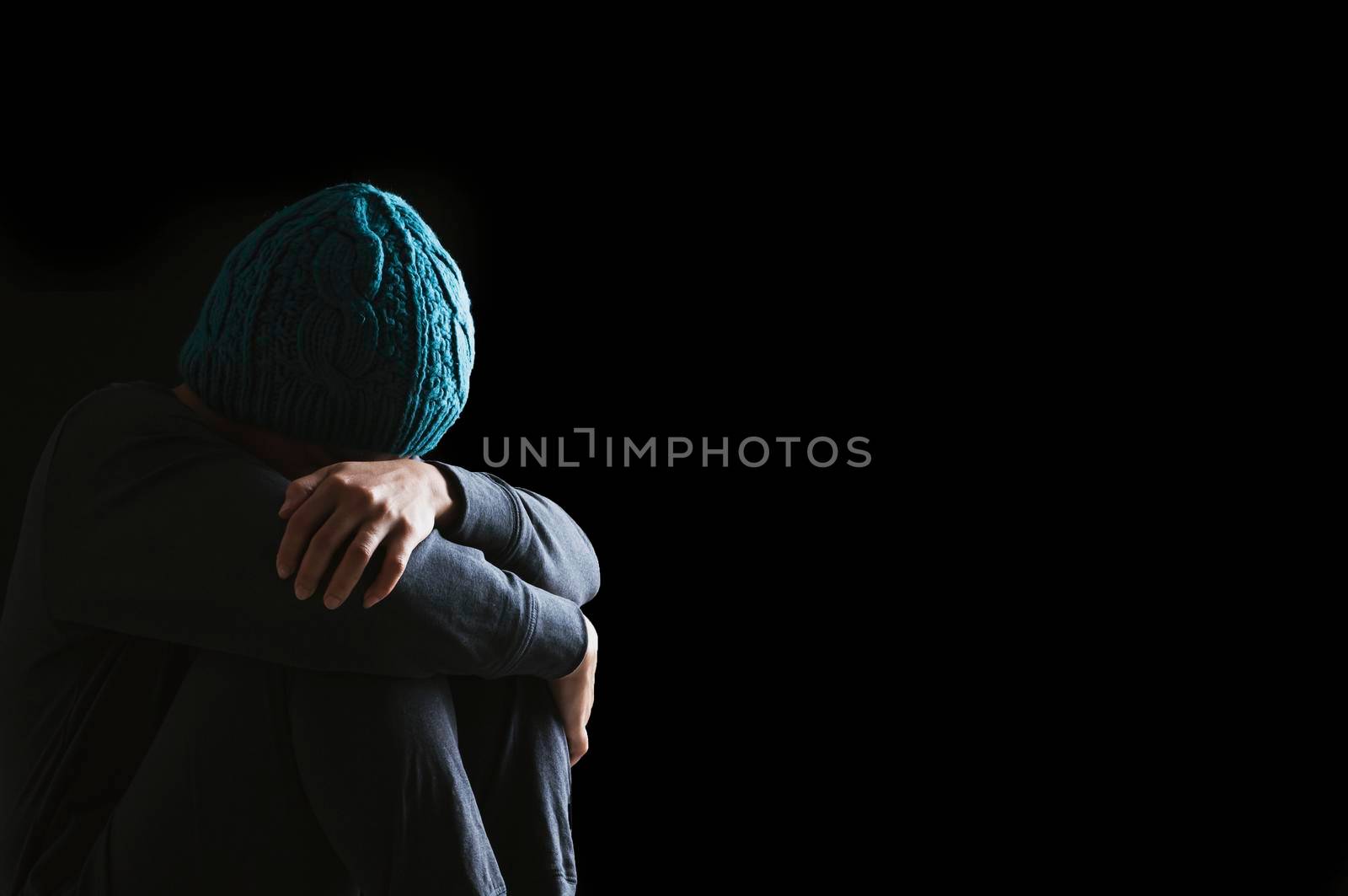Sad woman hug her knee with depression sitting alone on the floor in the dark room, Black background by thanumporn