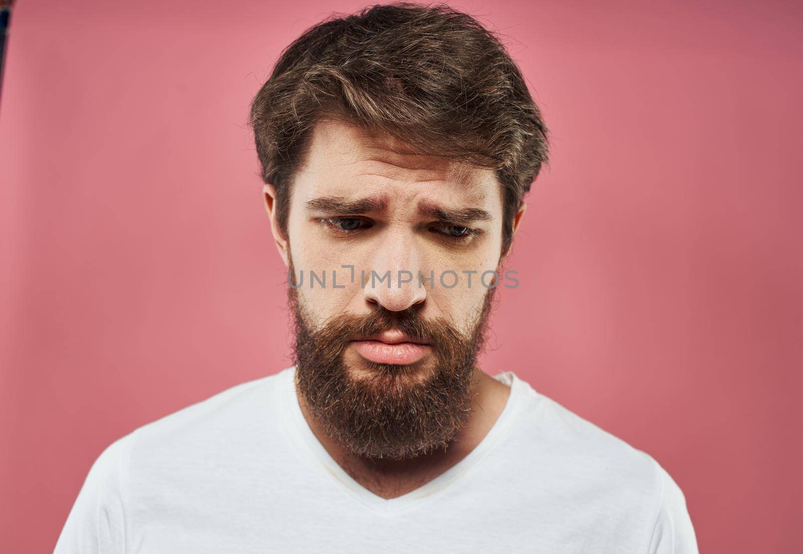 Sad man crying on a pink background in a white t-shirt cropped view. High quality photo