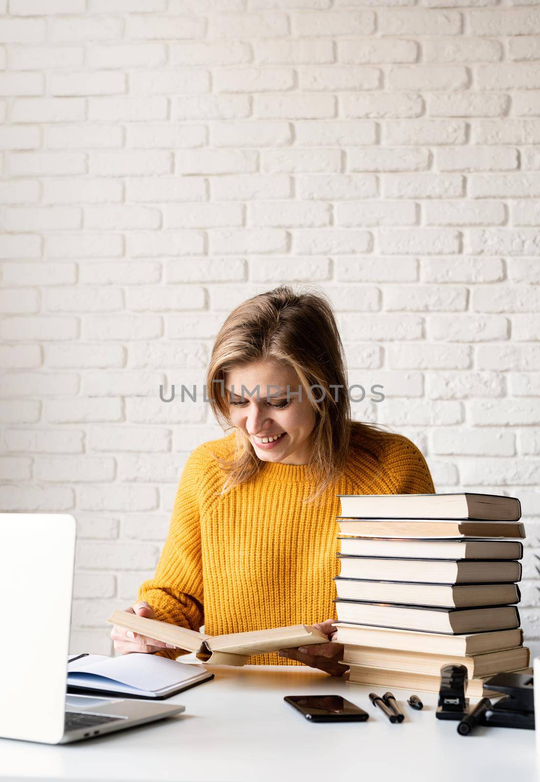 Young smiling woman in yellow sweater studying reading a book by Desperada