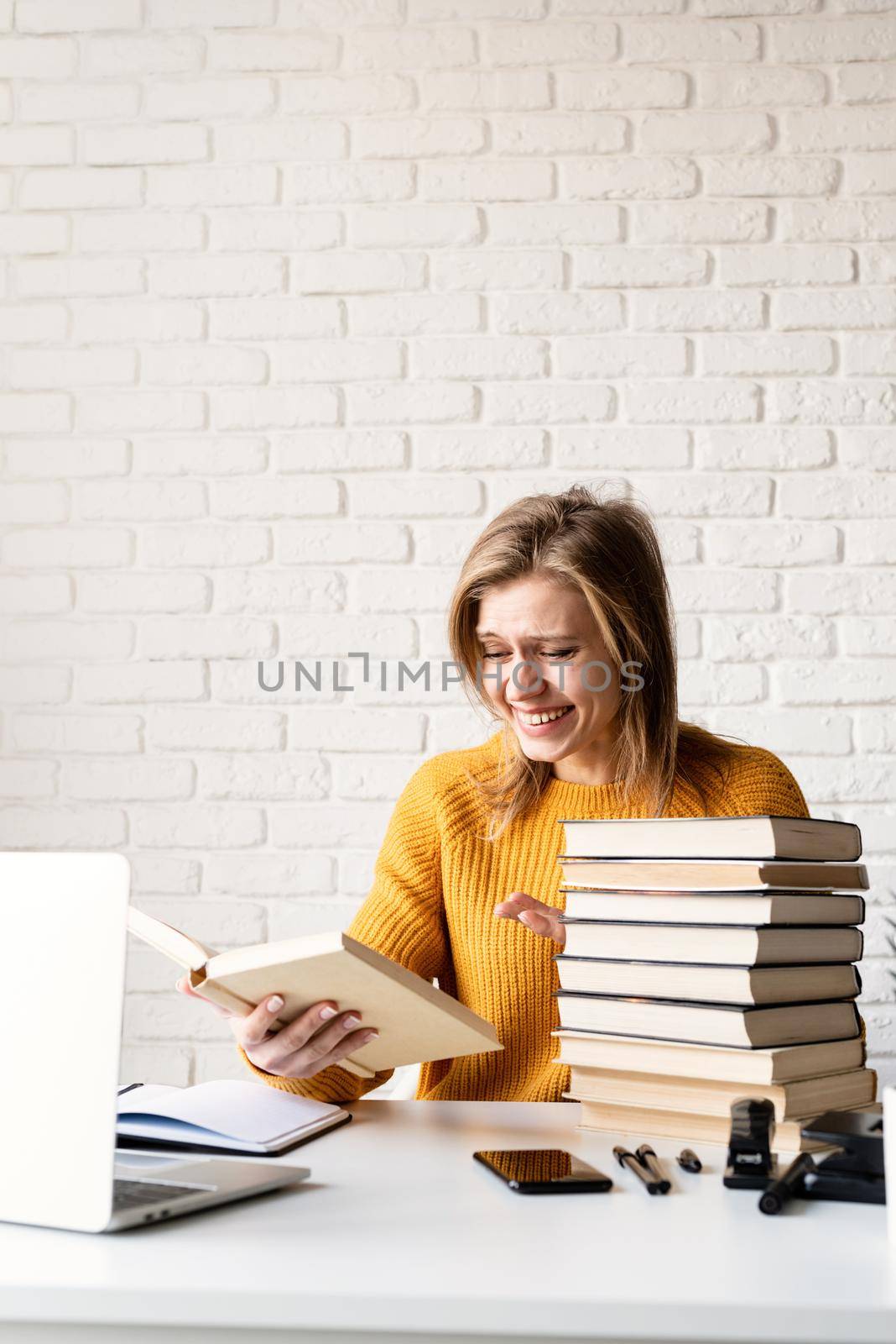 Young smiling woman in yellow sweater reading a book and laughing by Desperada