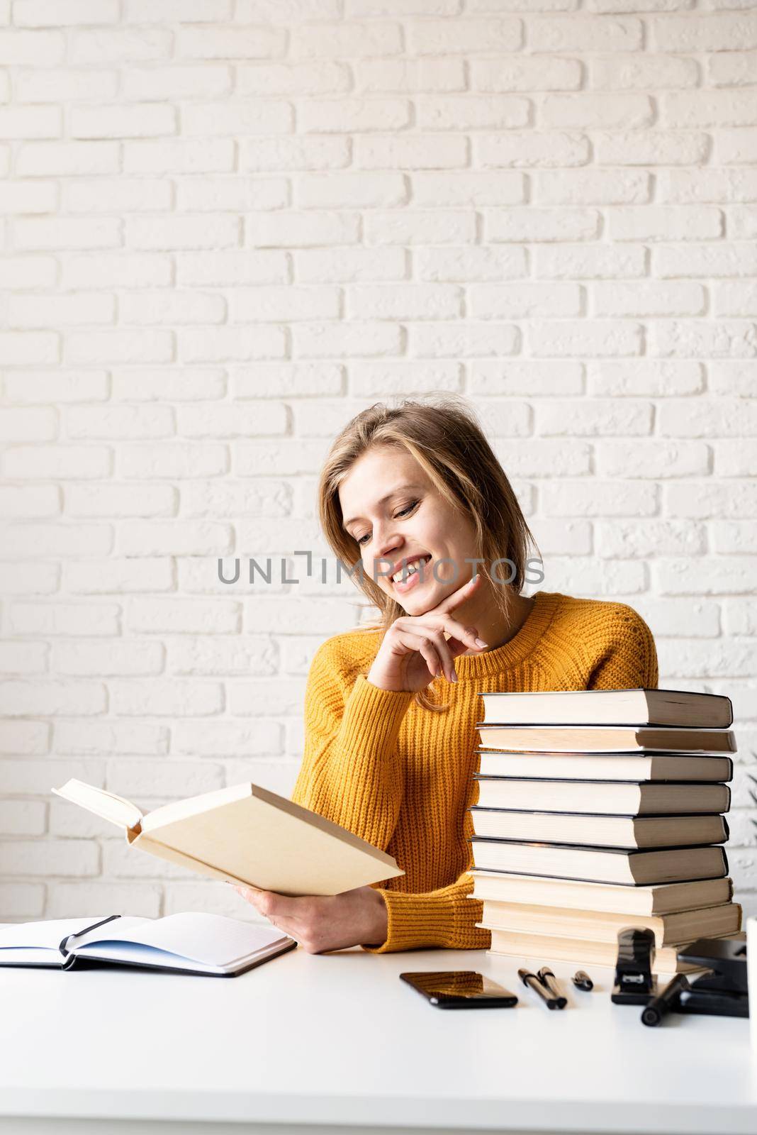 Young smiling woman in yellow sweater laughing reading a book