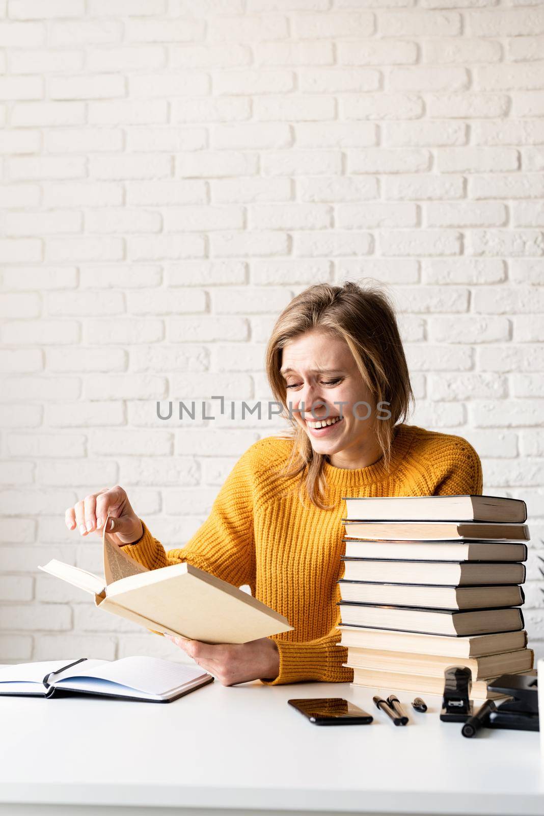 Young smiling woman in yellow sweater reading a book and laughing by Desperada