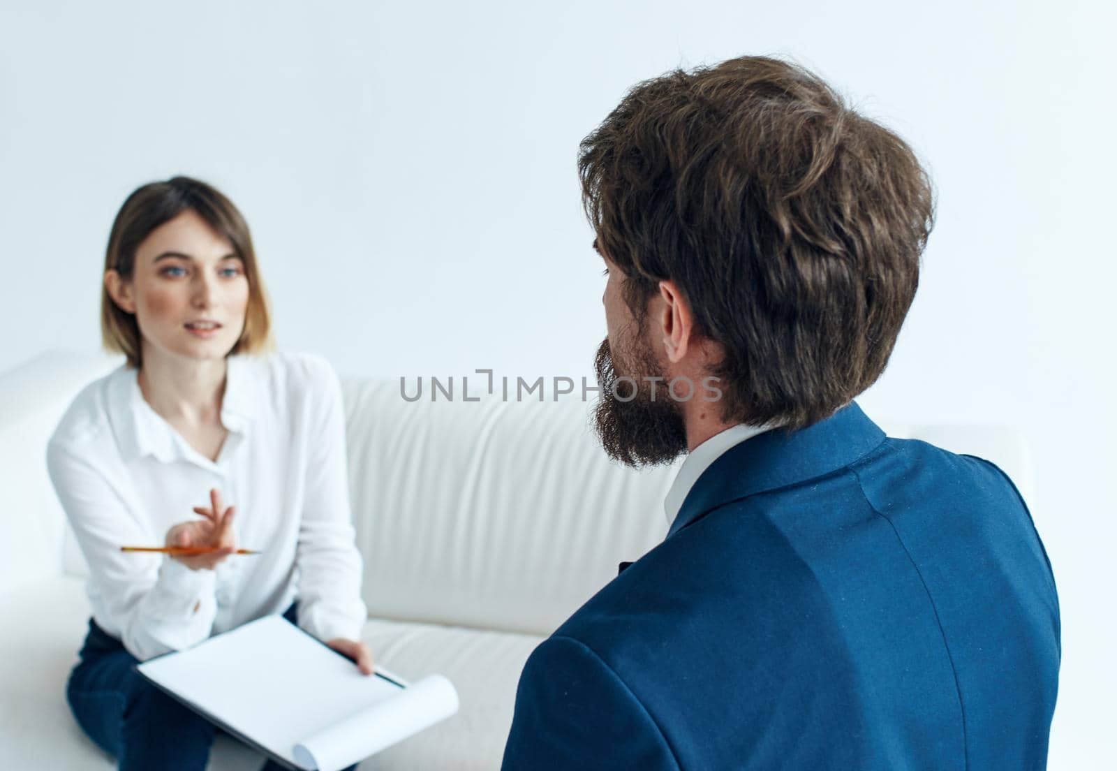 A man in a blue jacket and a beard talks to a woman on the sofa indoors by SHOTPRIME
