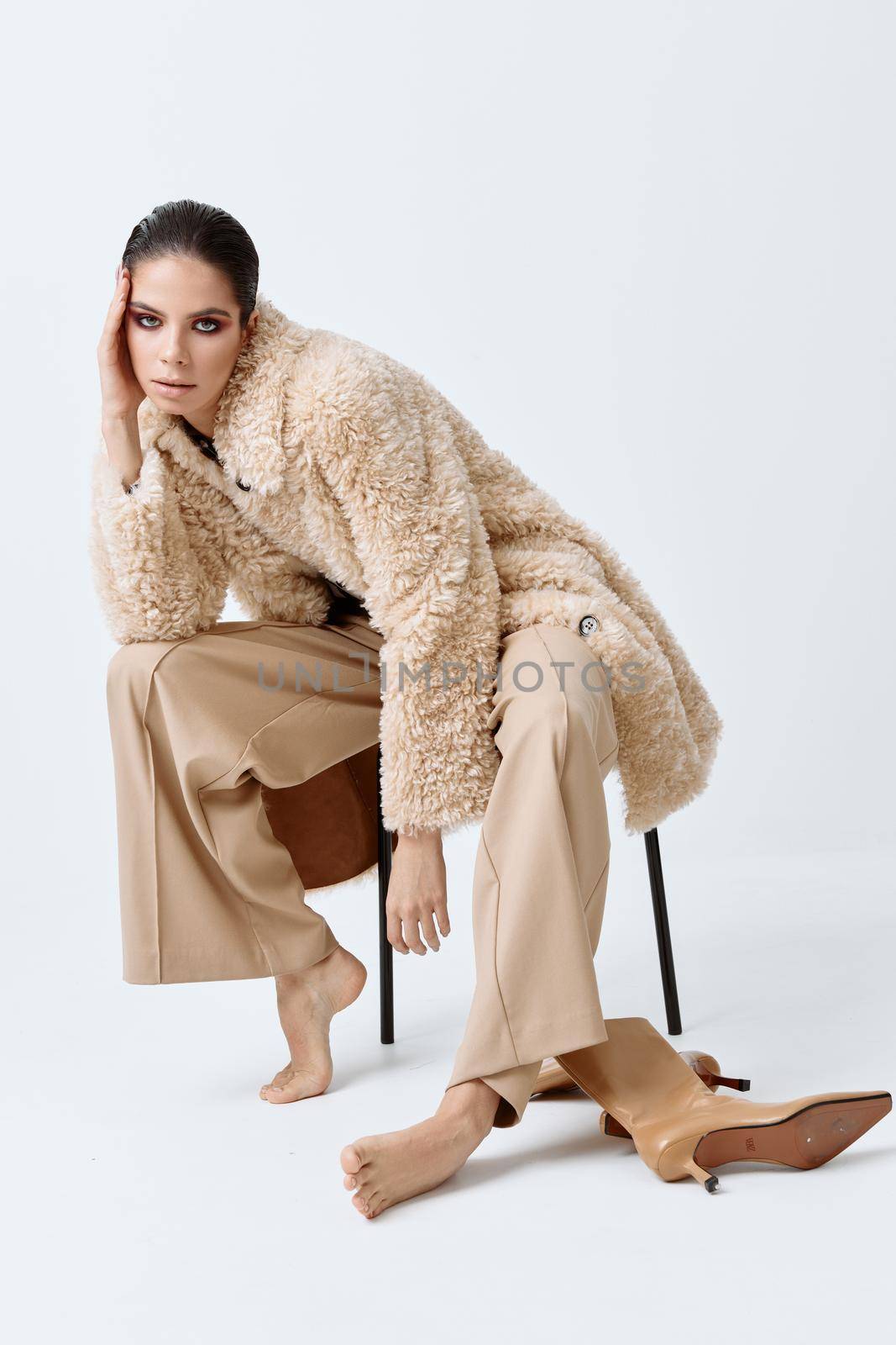 brunette with bright makeup on her face beige coat fashionable clothes barefoot sitting on a chair. High quality photo