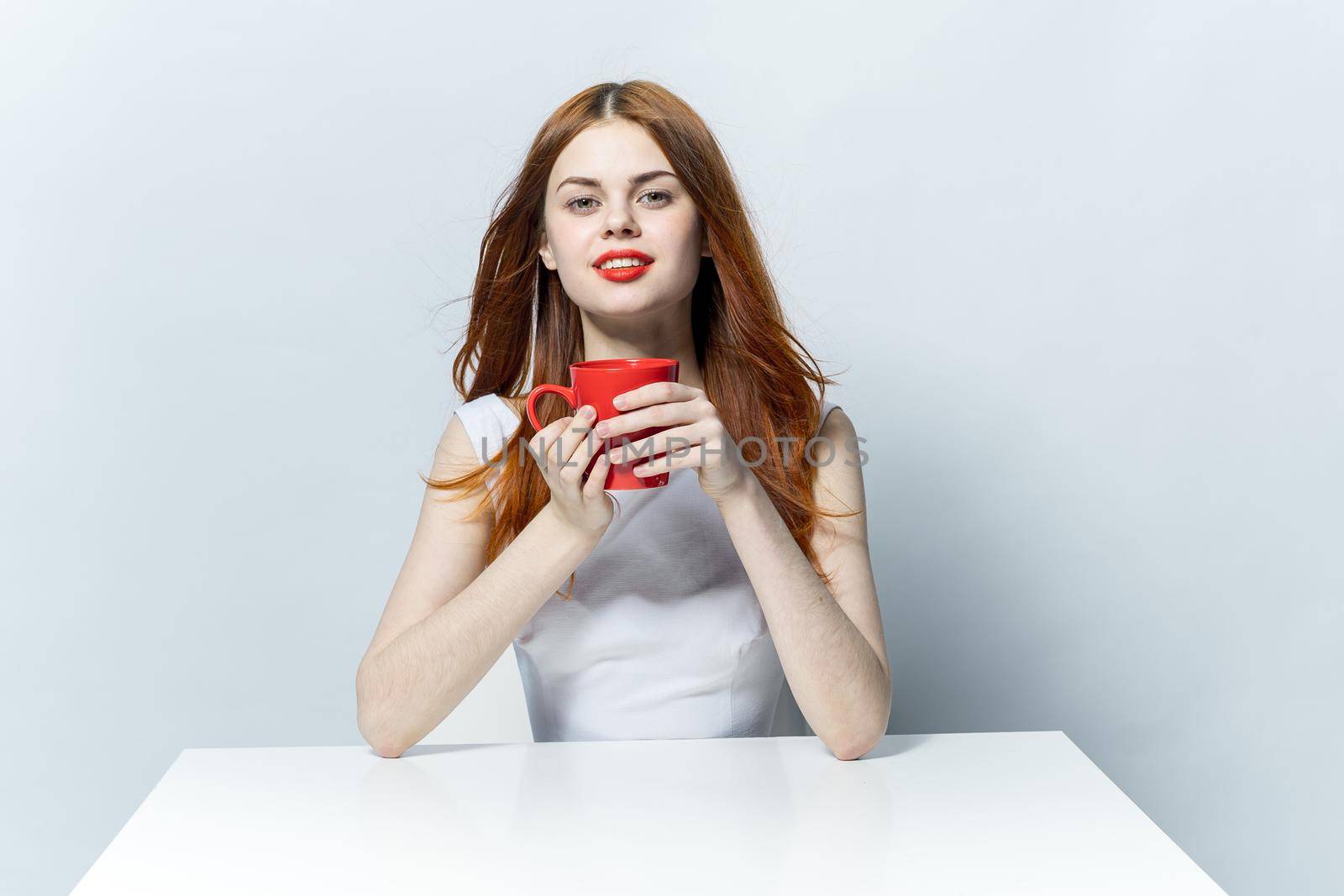 pretty woman at the table with red mug in hands charm . High quality photo