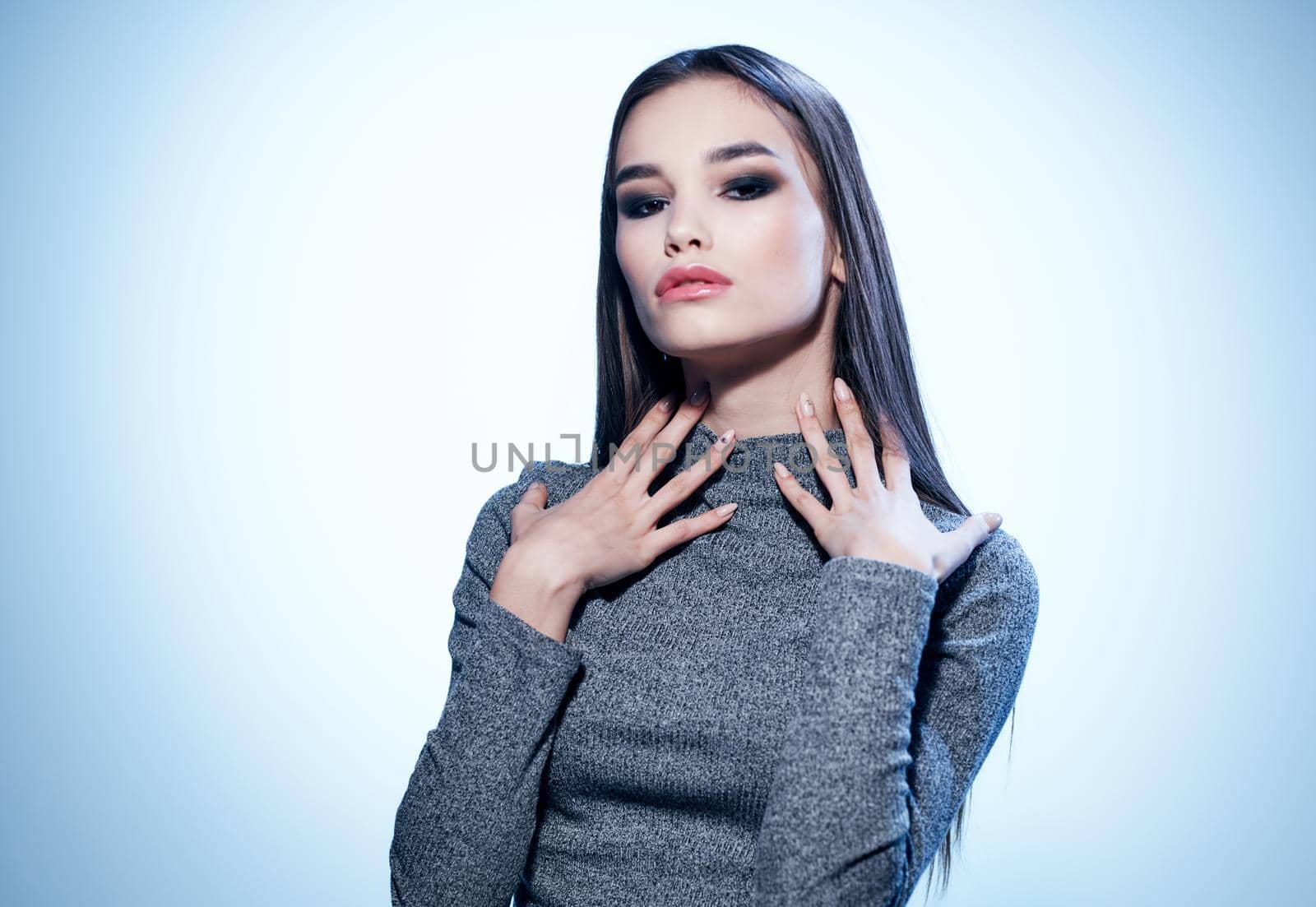 An elegant lady in a gray sweater gestures with her hands with makeup and eyeshadows. High quality photo