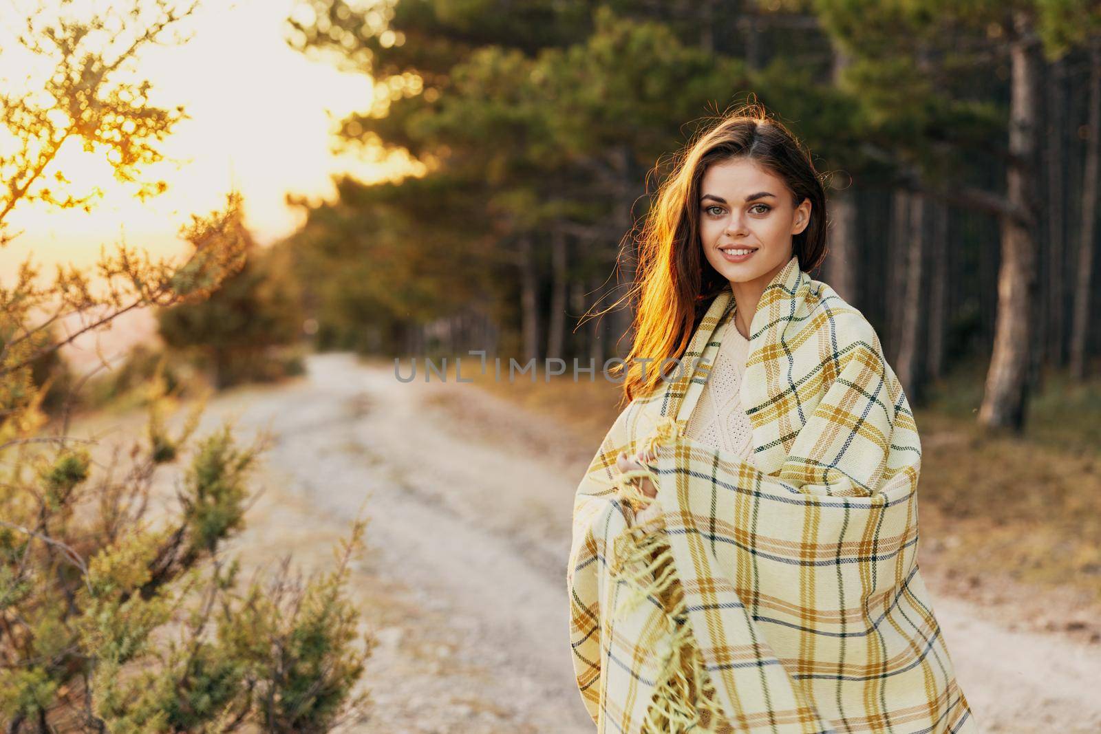 Happy woman tourist with a plaid on her shoulders near the coniferous forest. High quality photo