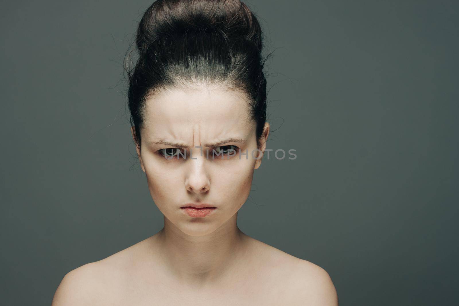 pretty woman with bare shoulders displeased look clear skin gray background. High quality photo