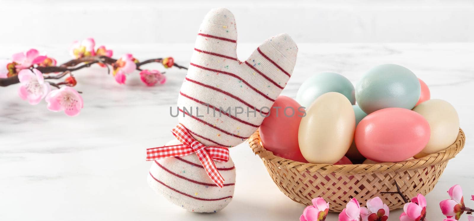 Close up of colorful Easter eggs in the nest with pink plum flower on bright white wooden table background.