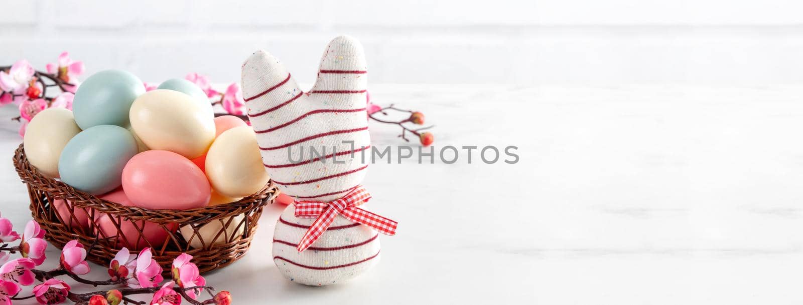 Close up of colorful Easter eggs in the nest with pink plum flower on bright white wooden table background.