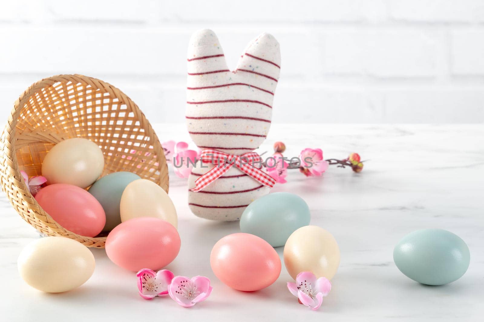 Close up of colorful Easter eggs in the nest with pink plum flower on bright white wooden table background.