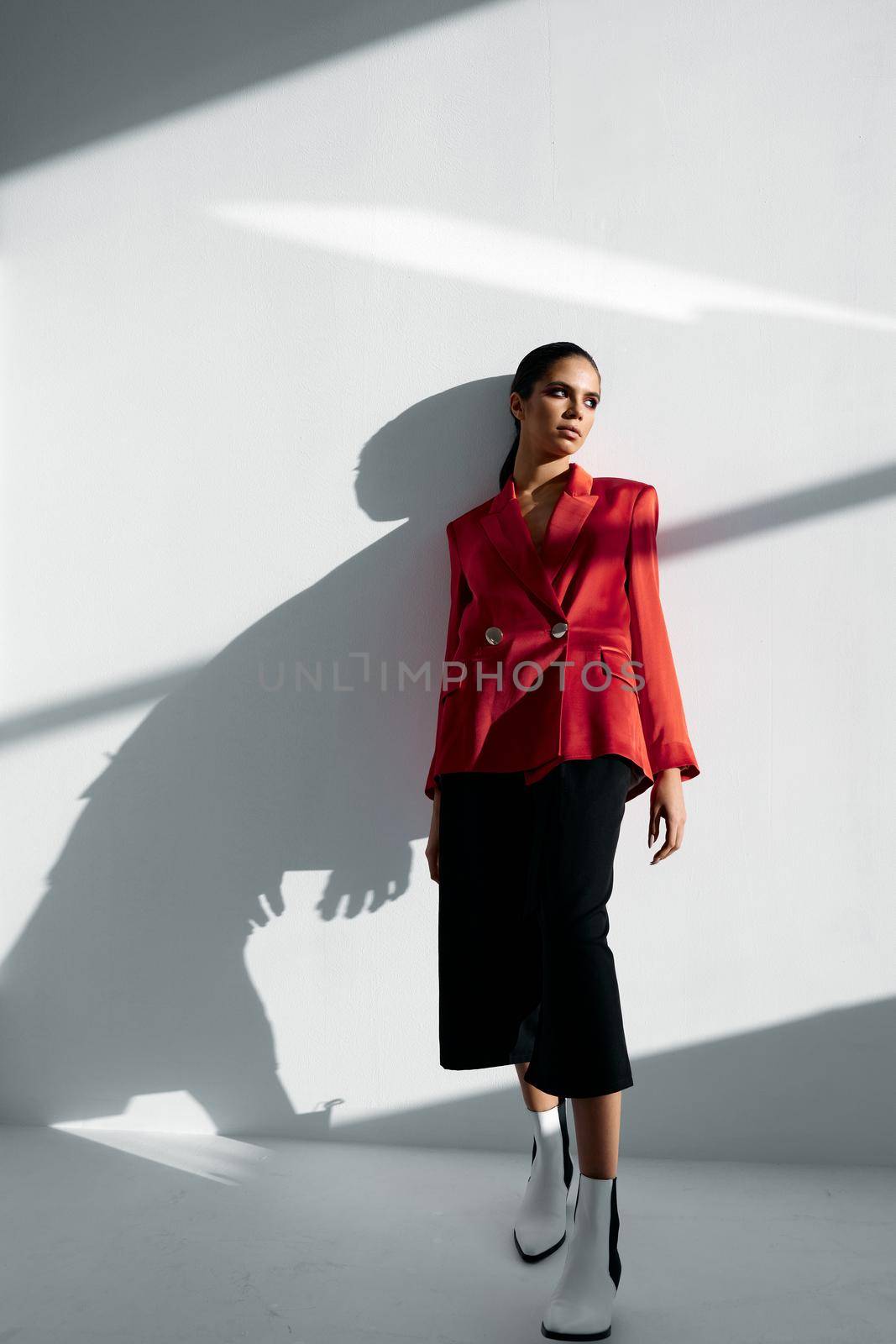 a woman in a fashionable suit is leaning against the wall in the room. High quality photo