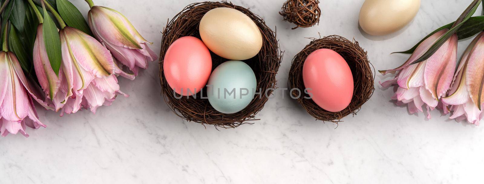 Colorful Easter eggs in the nest with pink lily flower on bright marble white table background.