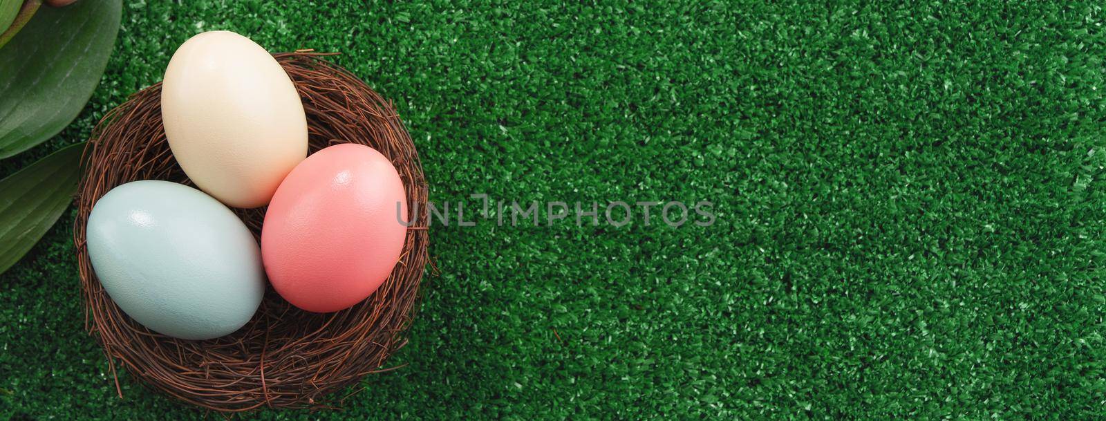 Colorful Easter eggs in the nest with pink lily flower on a lawn grass background.