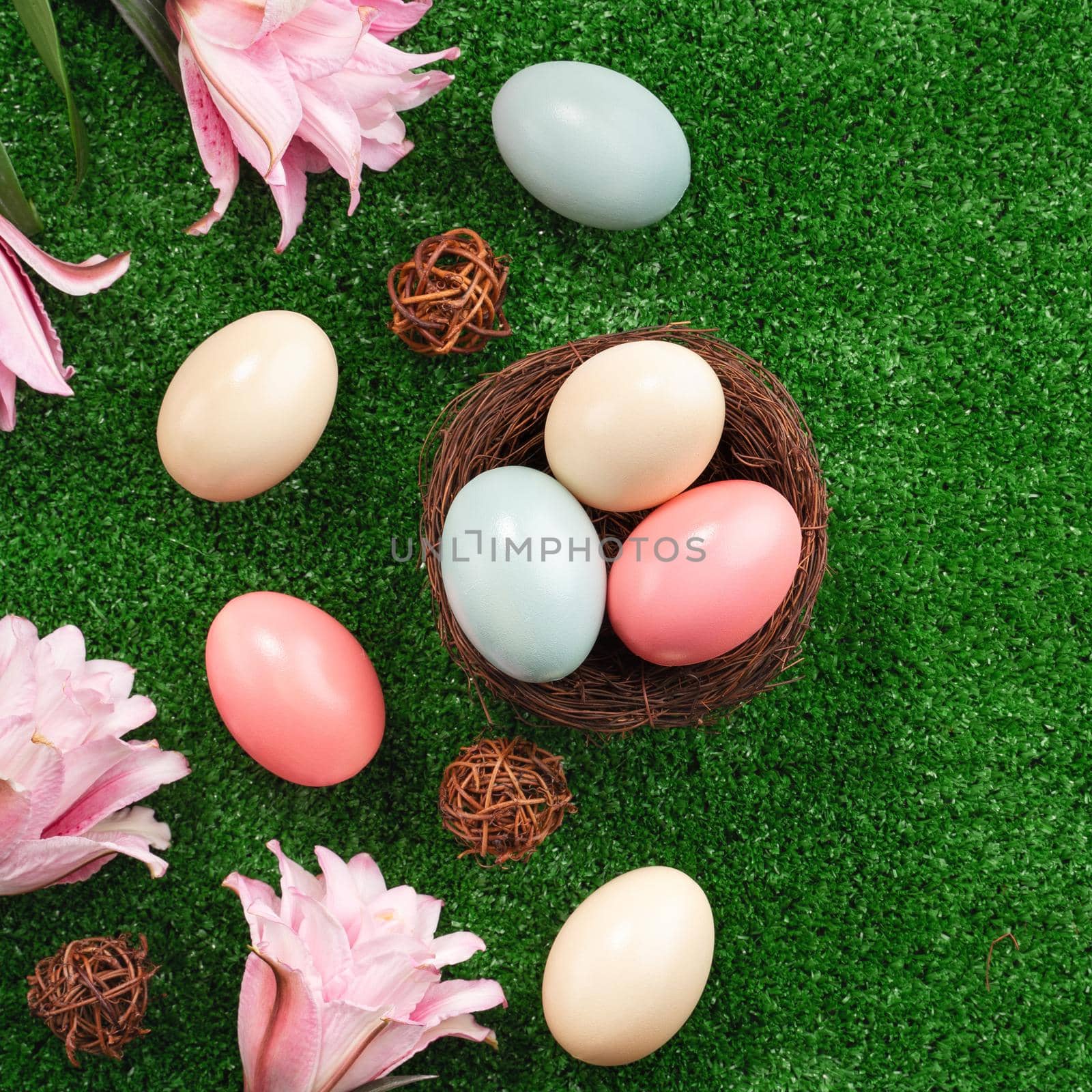 Colorful Easter eggs in the nest with pink lily flower on a lawn grass background.