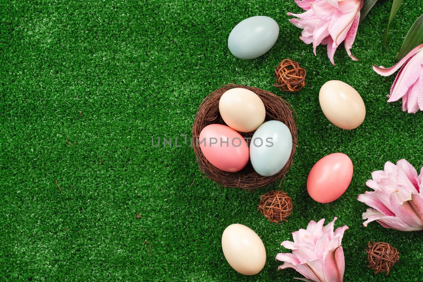 Colorful Easter eggs in the nest with pink lily flower on a lawn grass background.