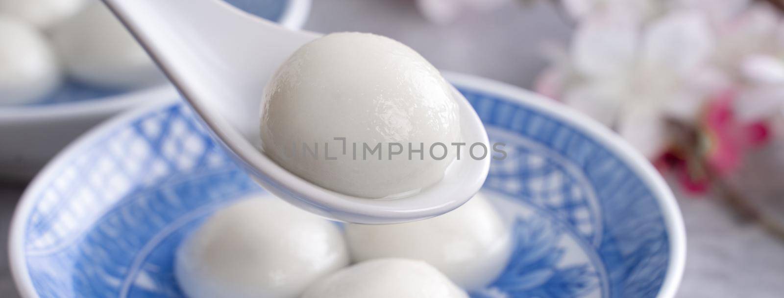 Close up of yuanxiao tangyuan (glutinous rice dumpling balls) in a bowl on gray table with flower, food for Chinese Lantern Yuanxiao Festival.
