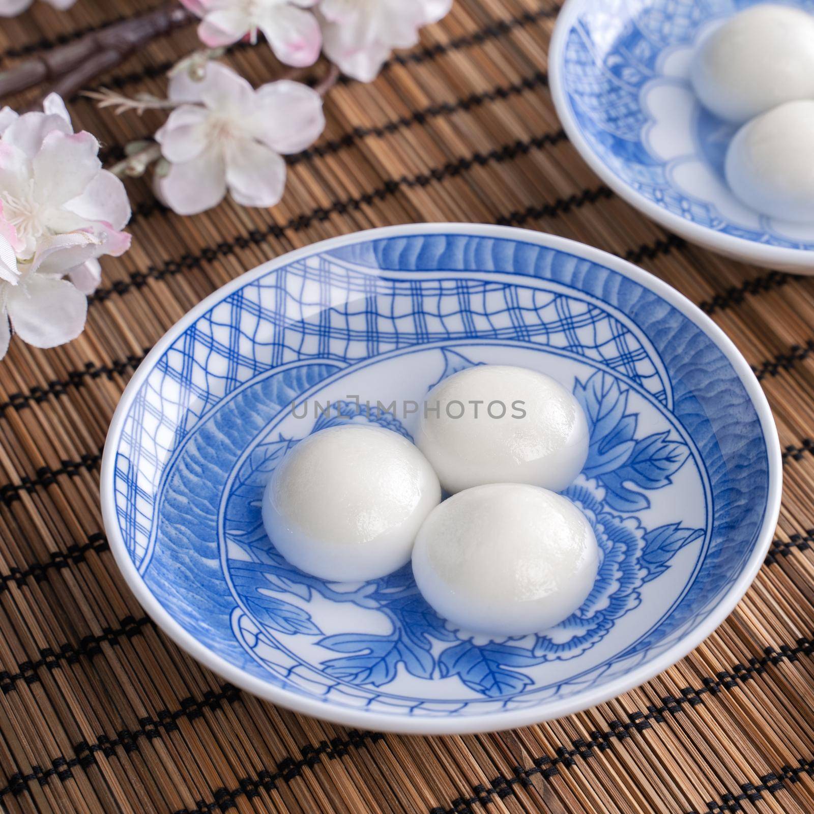 Close up of yuanxiao tangyuan (glutinous rice dumpling balls) in a bowl on gray table with flower, food for Chinese Lantern Yuanxiao Festival.