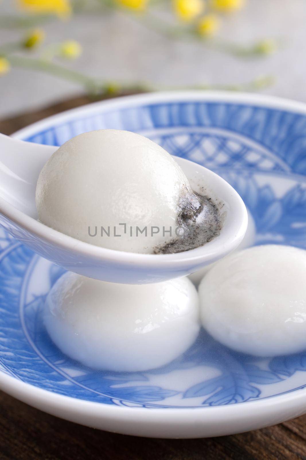Close up of yuanxiao tangyuan (glutinous rice dumpling balls) in a bowl on gray table with flower, food for Chinese Lantern Yuanxiao Festival.