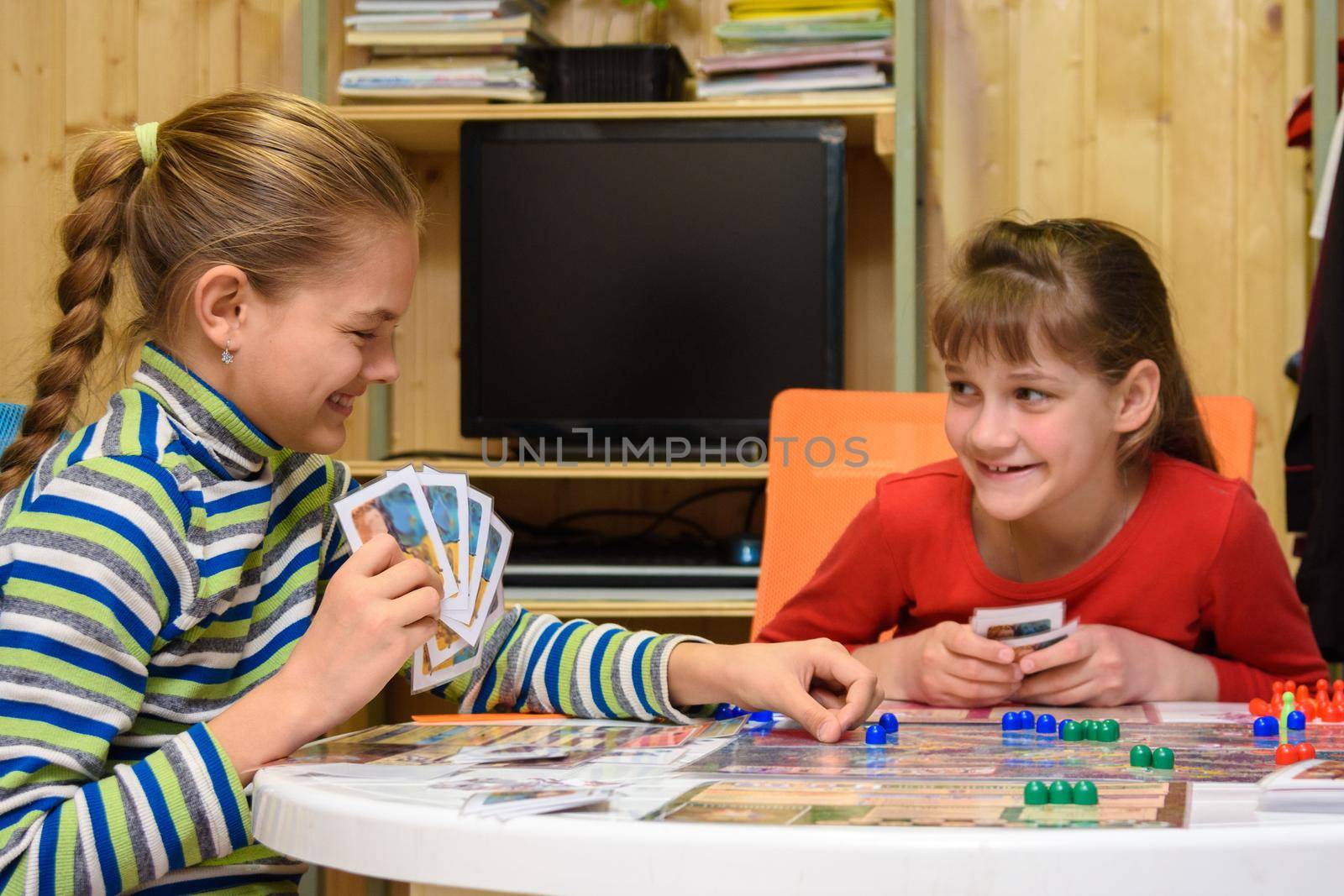 Two girls joyfully laugh while playing board games at the table
