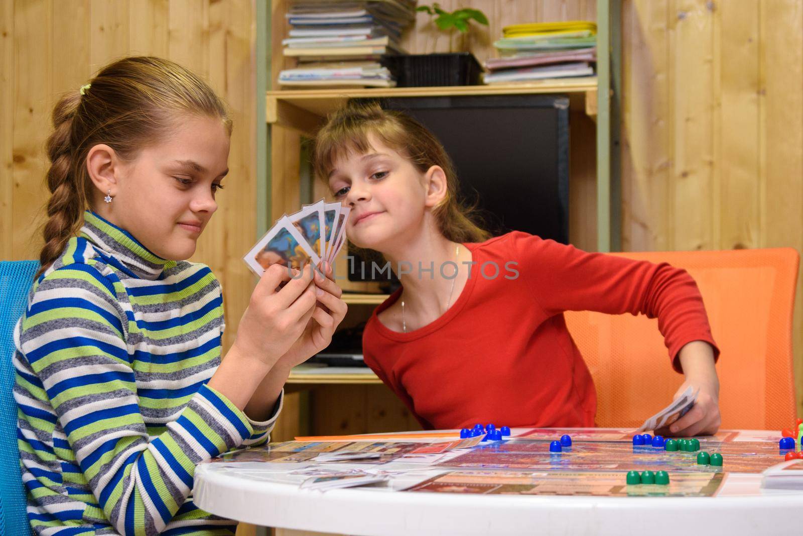Children play a board game, one of the girls peeps at the cards of the other