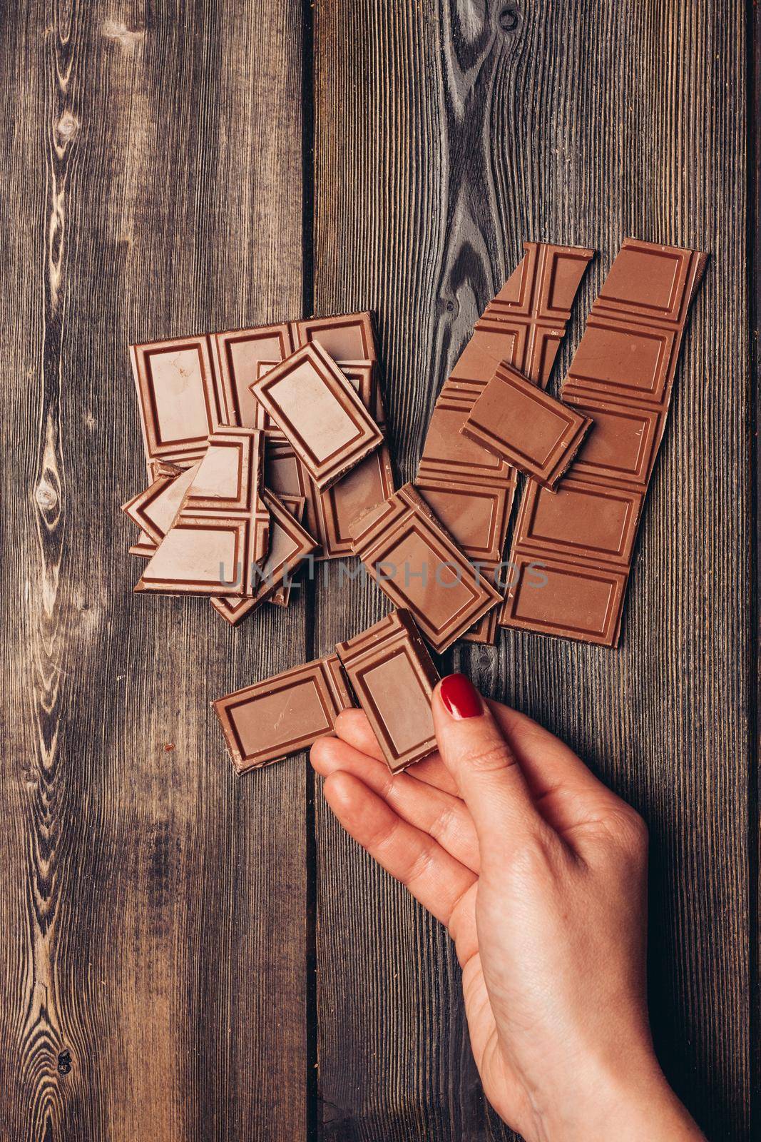 female hand and broken bar of chocolate on wooden table portrait by SHOTPRIME