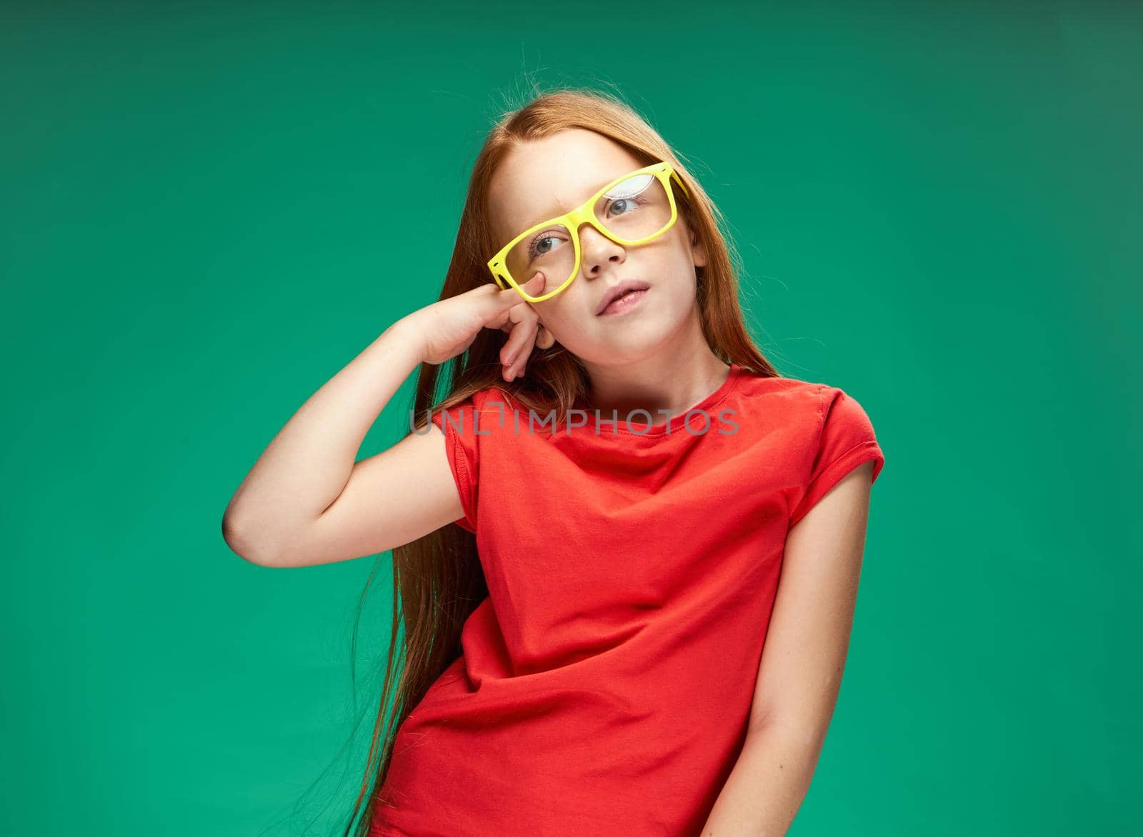 cute red-haired girl gesturing with her hands childhood green background school. High quality photo