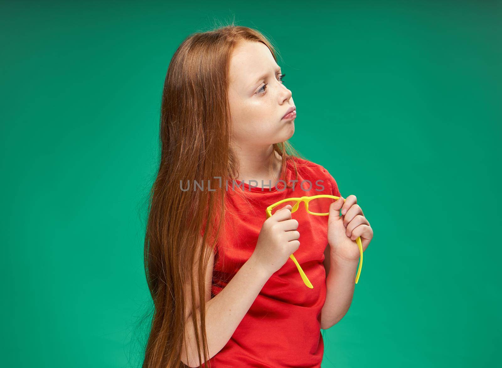 girl with red hair holding yellow glasses in her hands green background studio red t-shirt. High quality photo