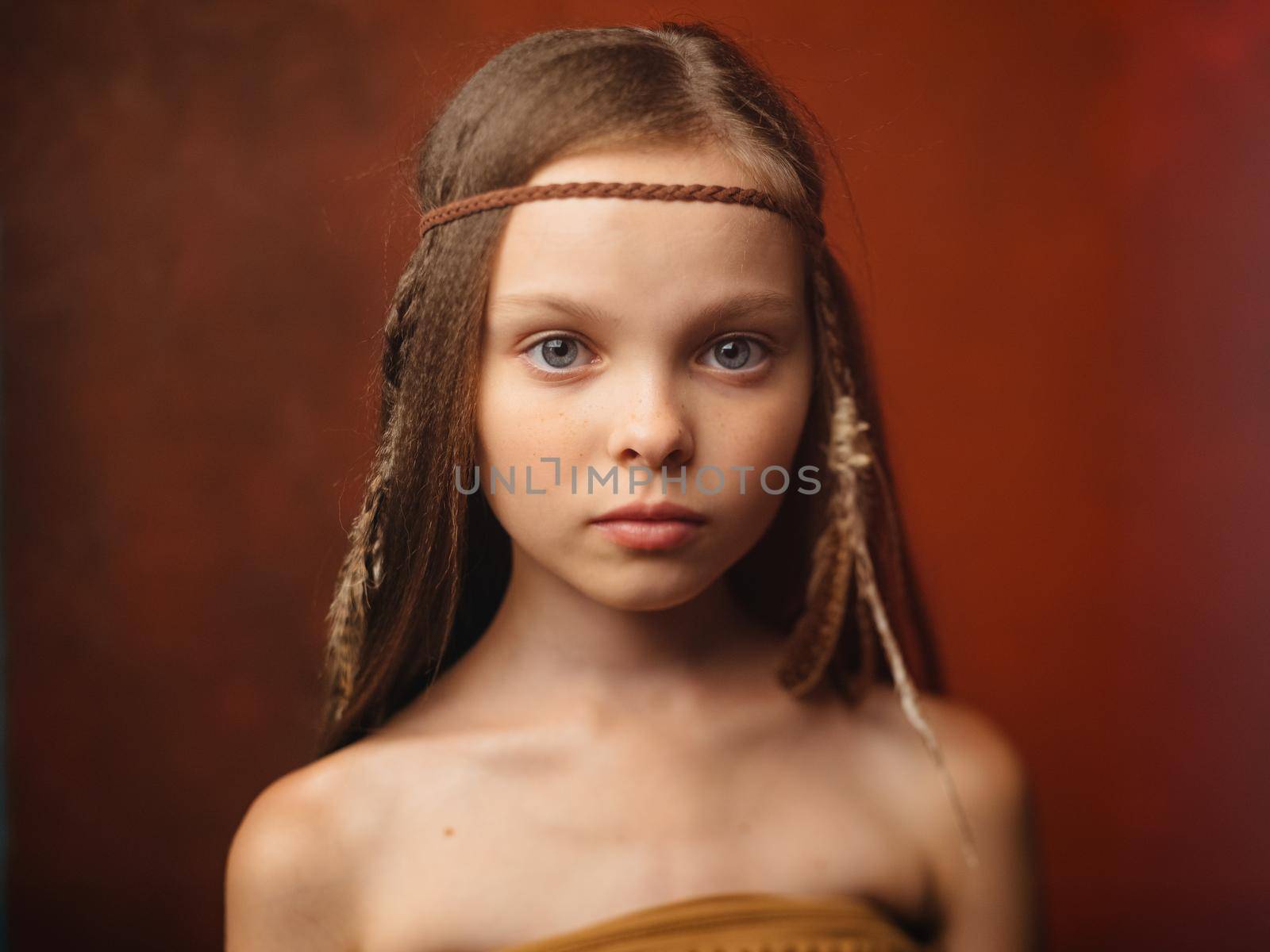 The girl on a red background with an ornament on the head of a feather aborigines savage. High quality photo