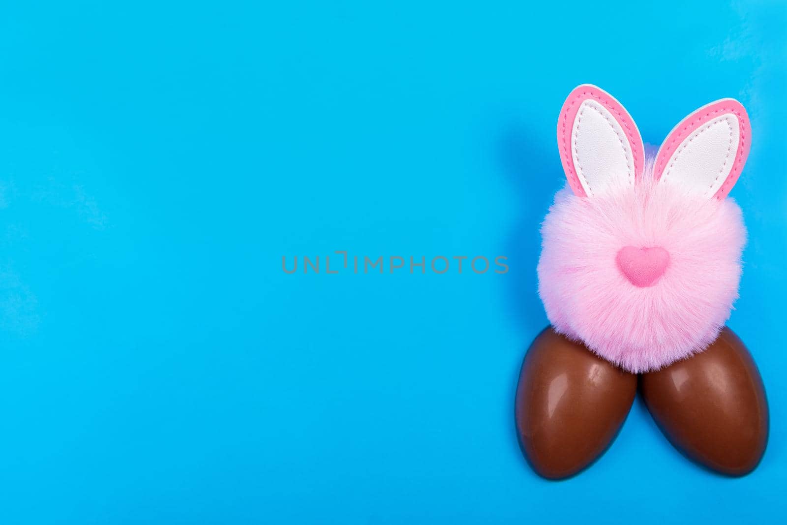 Easter, chocolate egg, pink toy rabbit head on a blue background. Place for text