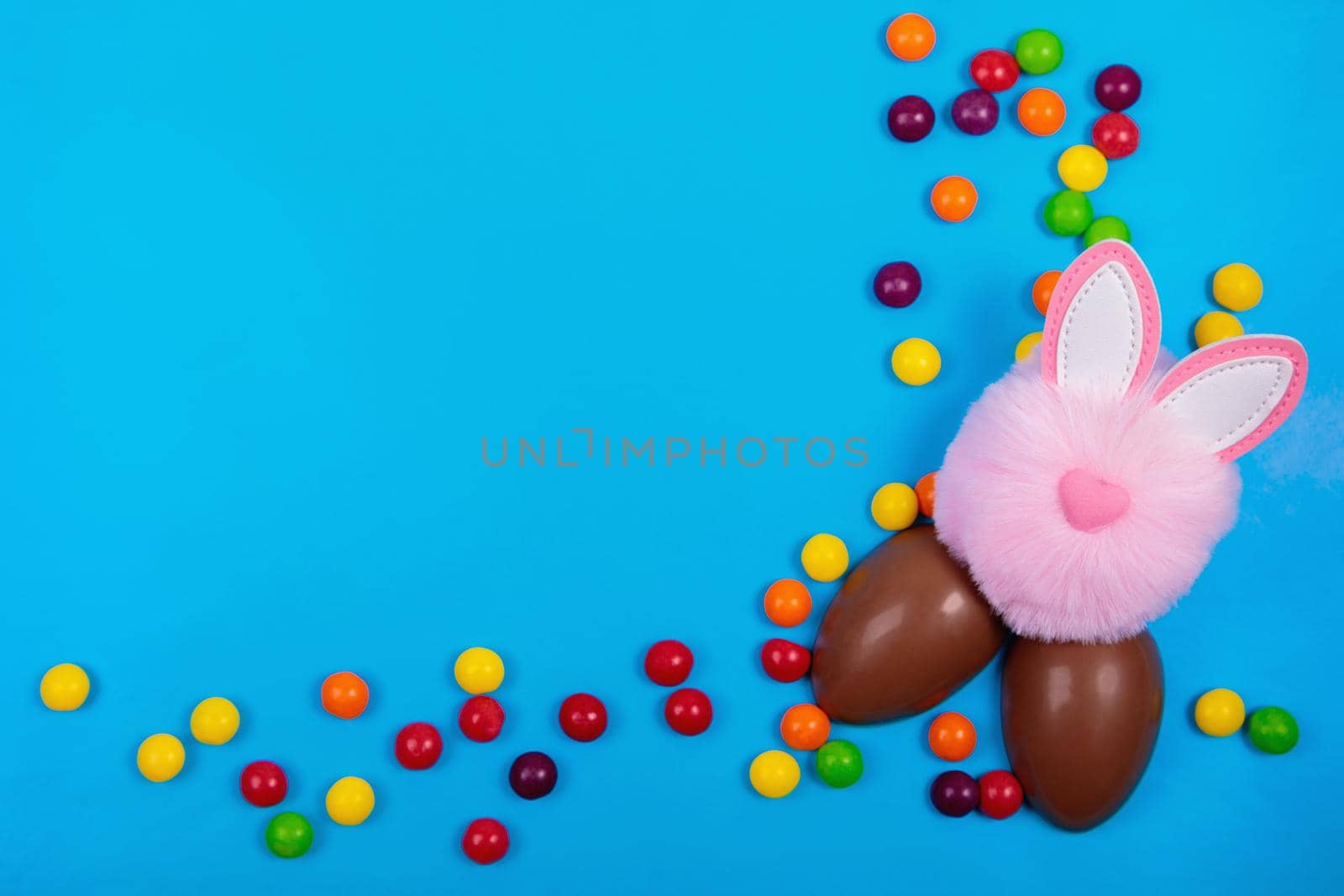Easter concept, candy jelly beans, chocolate egg, pink rabbit head toy on a blue background. Place for text