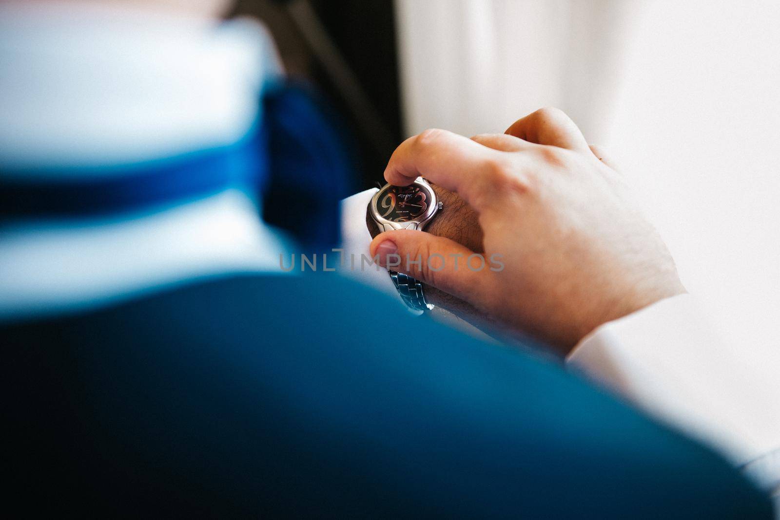 the groom in a blue suit looks at the watch worn on his left hand