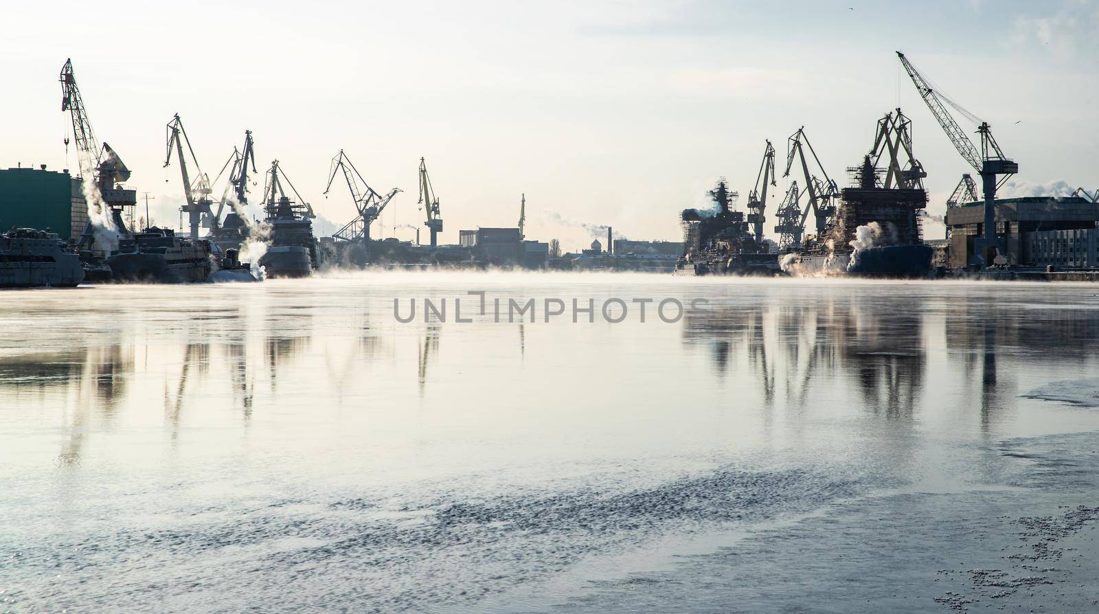 Cranes of of the Baltic shipyard on a frosty winter day, steam over the Neva river, smooth surface of the river, mirror reflection on the water, ships under construction, trawlers, nuclear icebreakers by vladimirdrozdin