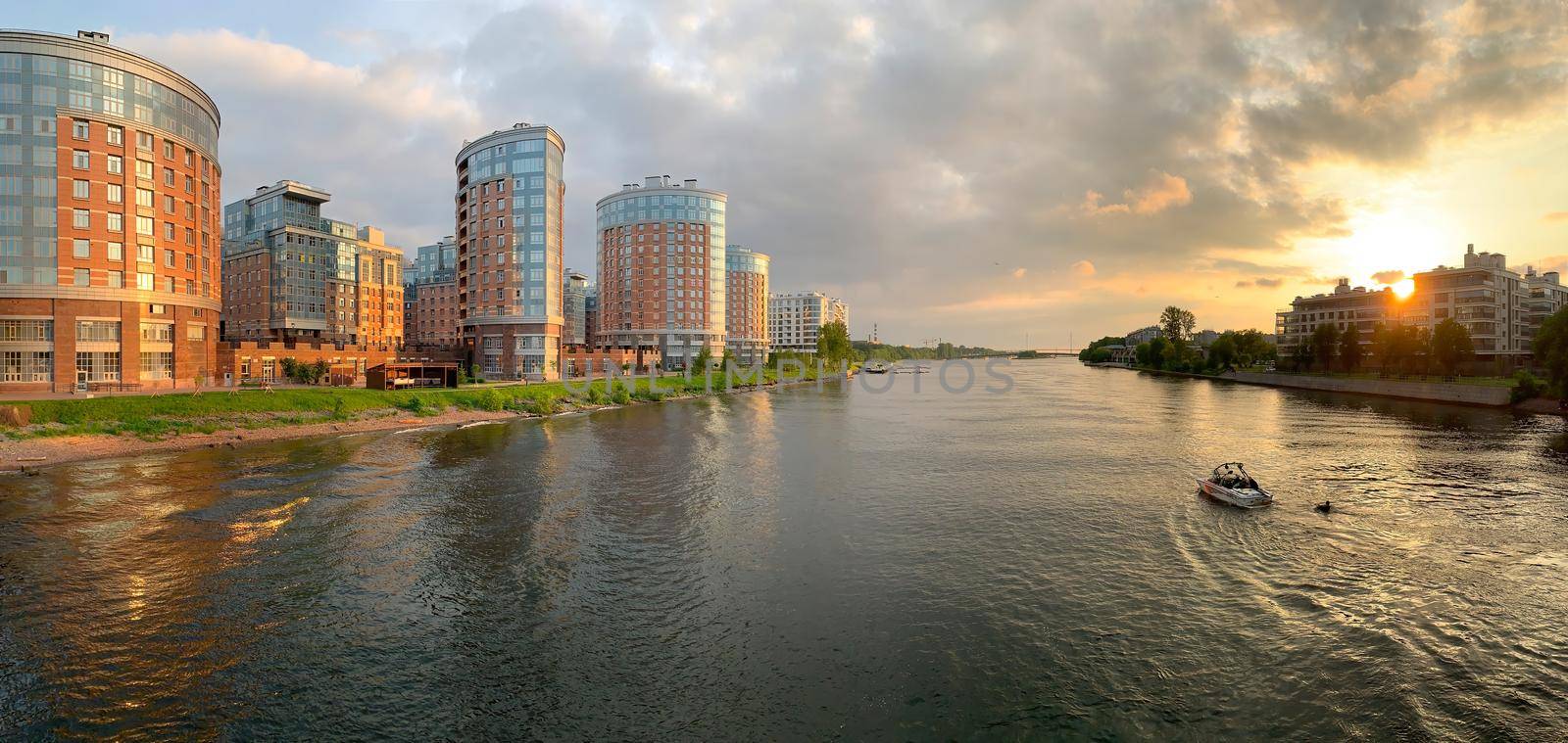 Russia, St.Petersburg, 10 June 2020: The boat with a wakesurfer on a wave goes down the river at sunset, a housing estate on a background, solar patches of light in windows of buildings