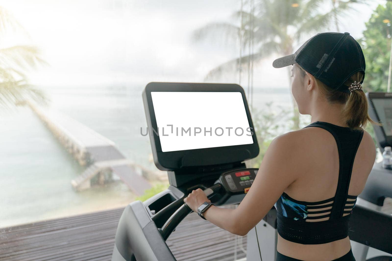 Woman is working out in gym. Doing cardio training on treadmill with white screen mockup , large windows with ocean view raining outside. by sirawit99