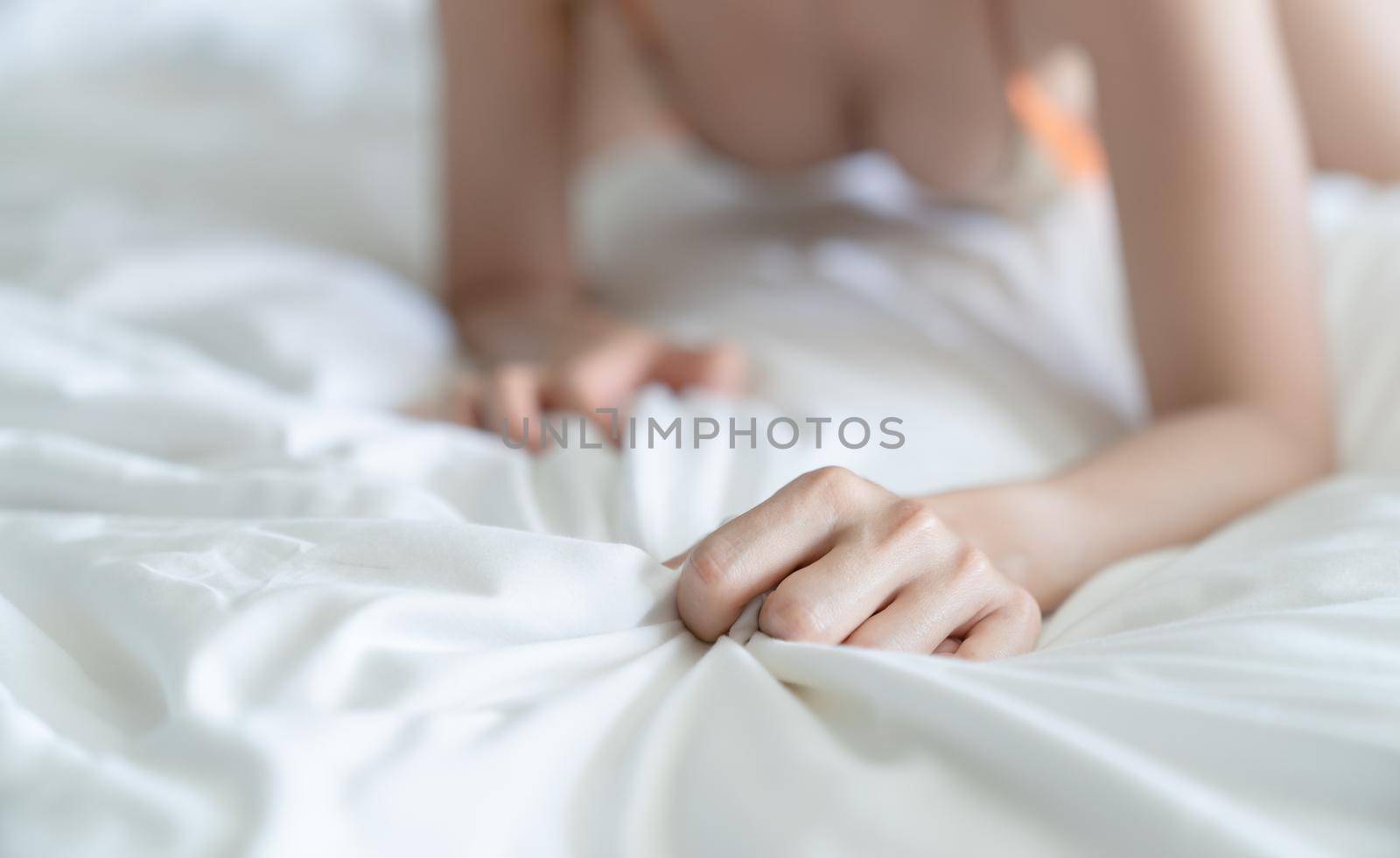Woman hand grasping white sheet. Couple making love or having sex in bedroom.