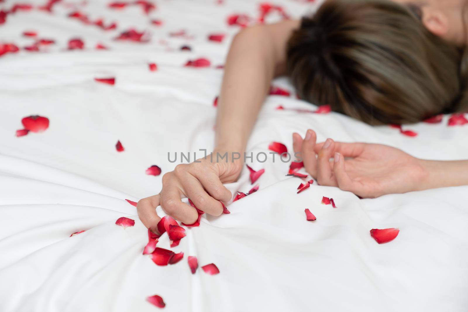 Women hand pulling or grasping white sheets. Hand sign orgasm of woman on white bed sheet with rose petals.