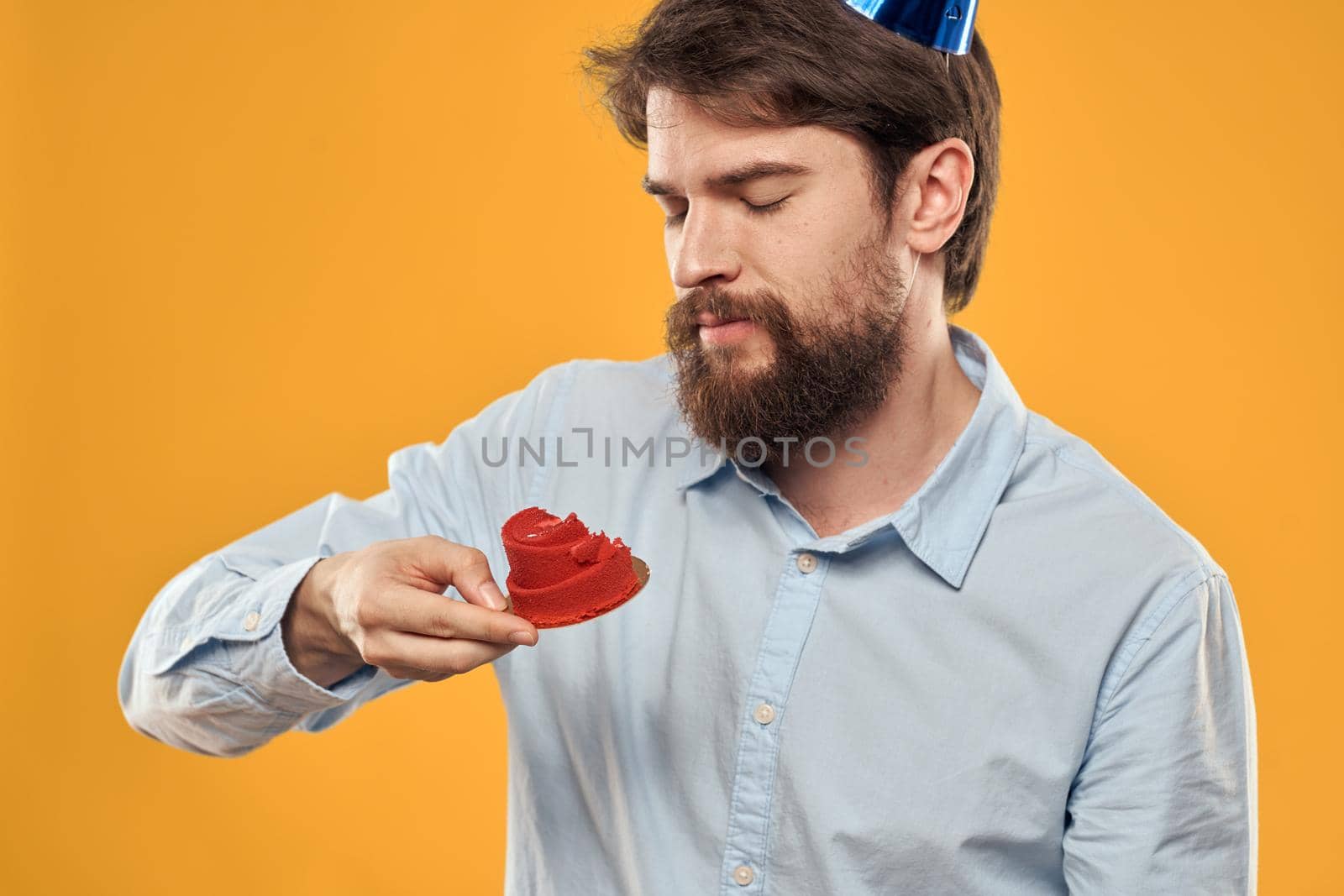 a man with a birthday cake in his hands and in a cap on a yellow background on his birthday. High quality photo