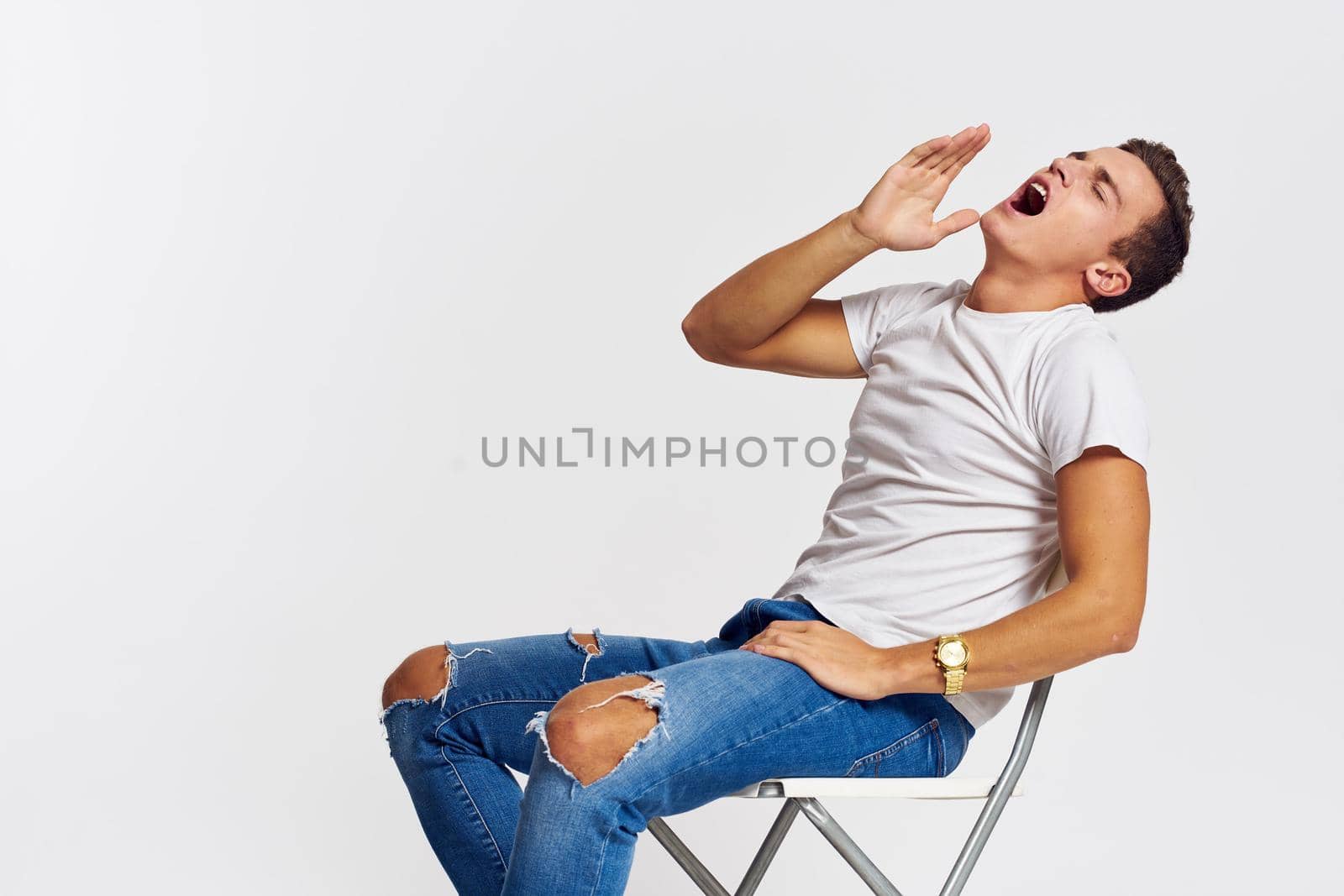 Man on a chair indoors torn jeans white t-shirt handsome face model light background. High quality photo