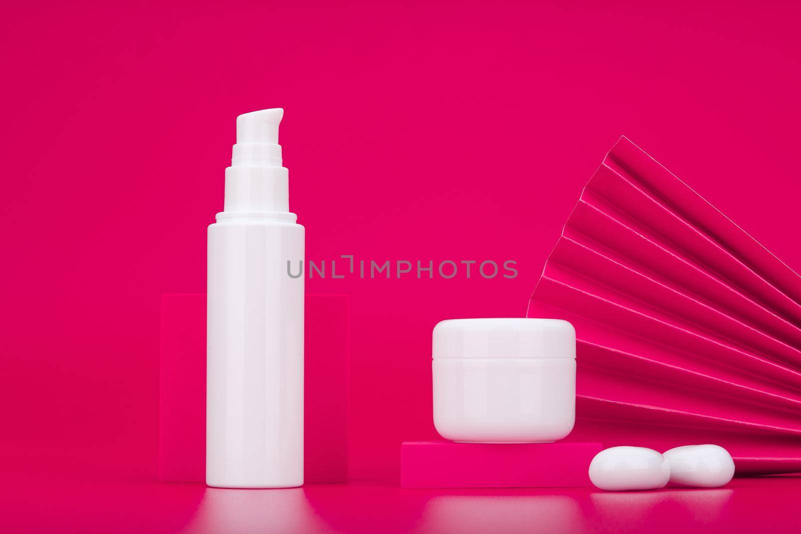 Face cream or lotion in white tube and under eye gel or lip balm in jar against pink background decorated with waver. Concept skin care and beauty in asian style or luxury skin care products