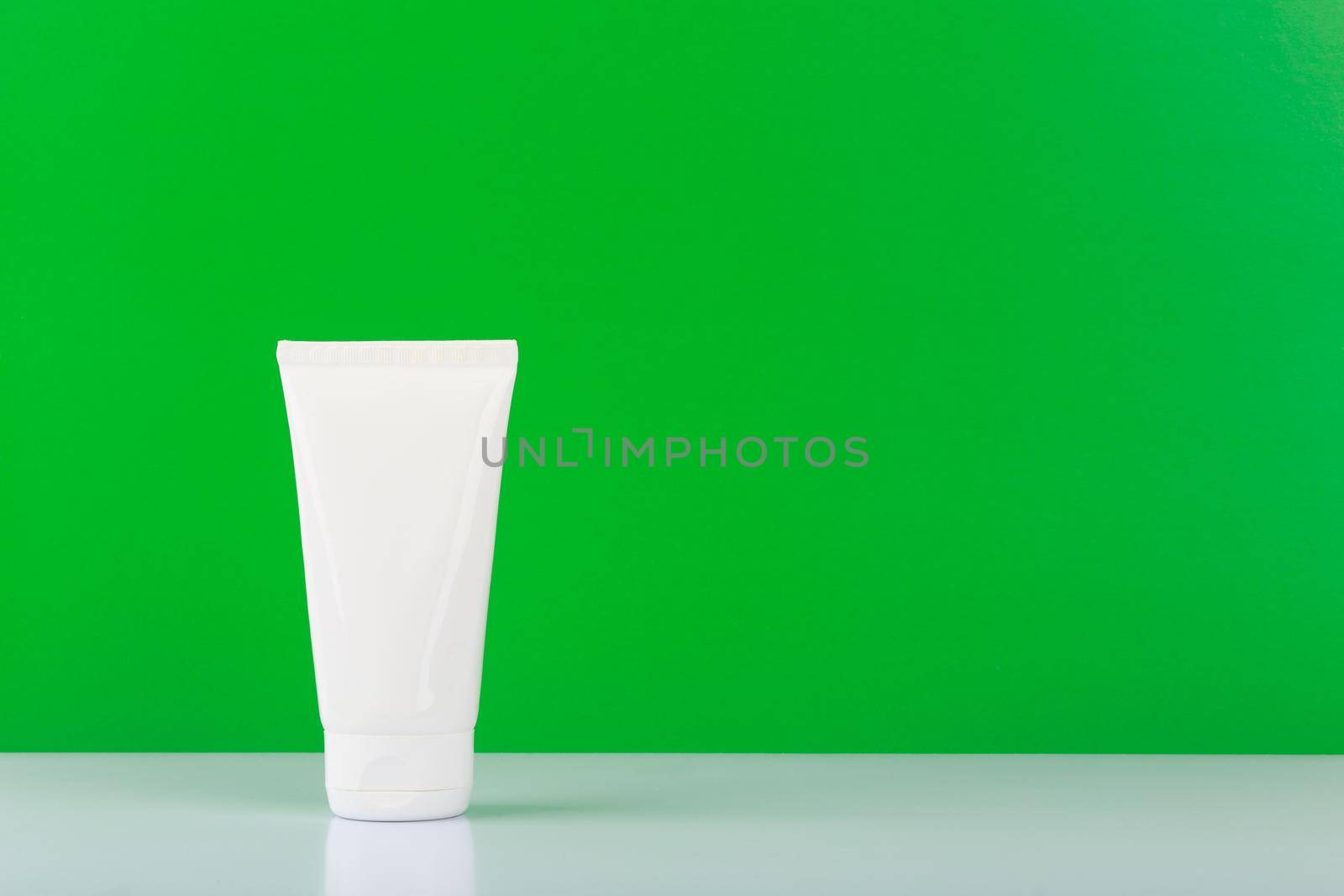 Hands cream in white plastic tube against green background with copy space. Concept of skin care product with natural ingredients and oils, aloe vera, cucumber or green tea. Moisturizing hands cream