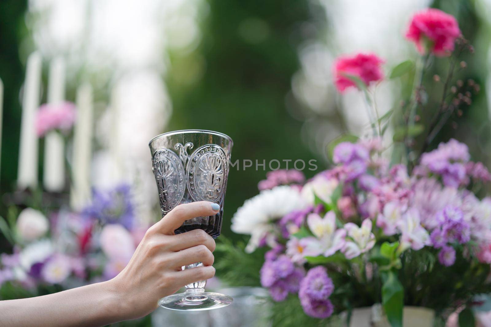 Glass of water in woman hand. Garden and flowers background.