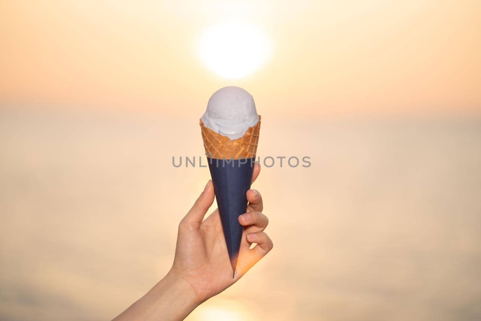 Scoop ice cream with a waffle cone in hand on the beach, sunset moment. by sirawit99