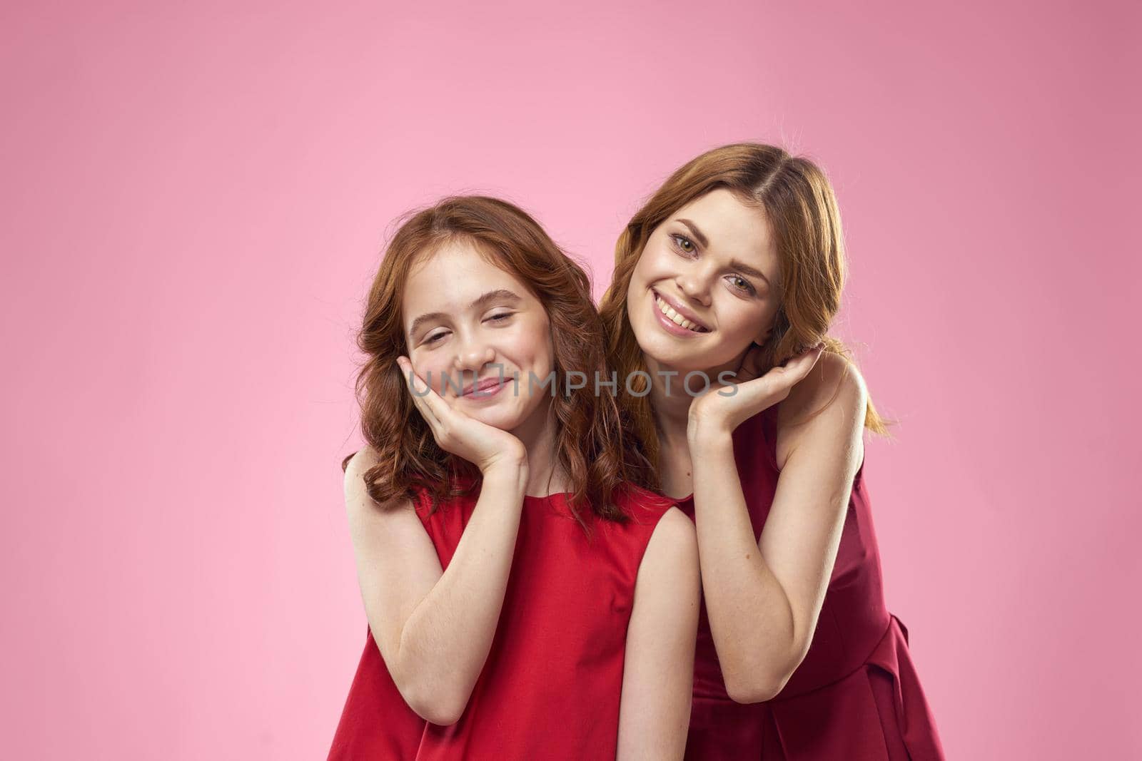 Cheerful mom and daughter wearing red dresses are standing next to joy family on pink background. High quality photo