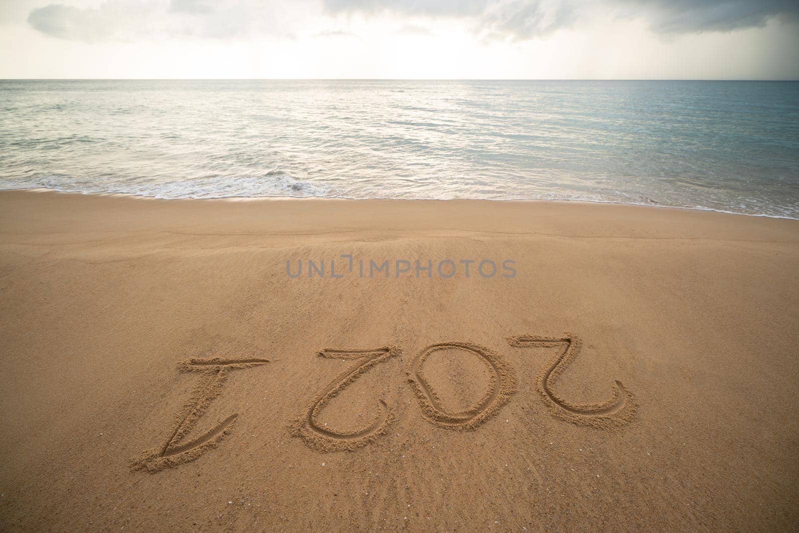 Handwriting year 2021 on sand and foam wave on beach. by sirawit99