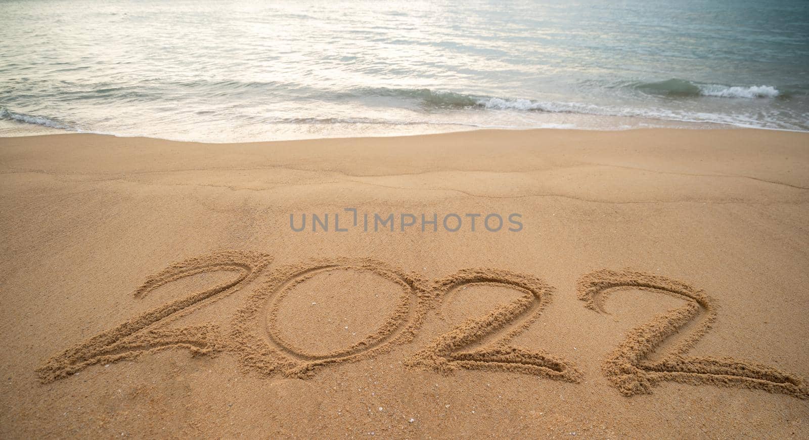 Handwriting year 2022 on sand and foam wave on beach.