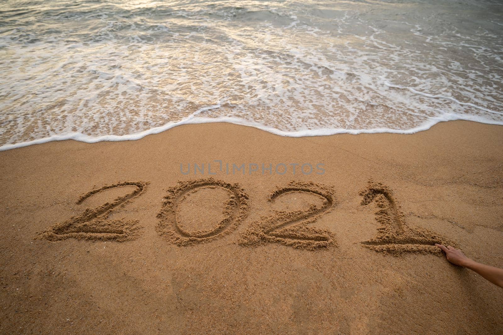 Handwriting year 2021 on sand and foam wave on beach. by sirawit99