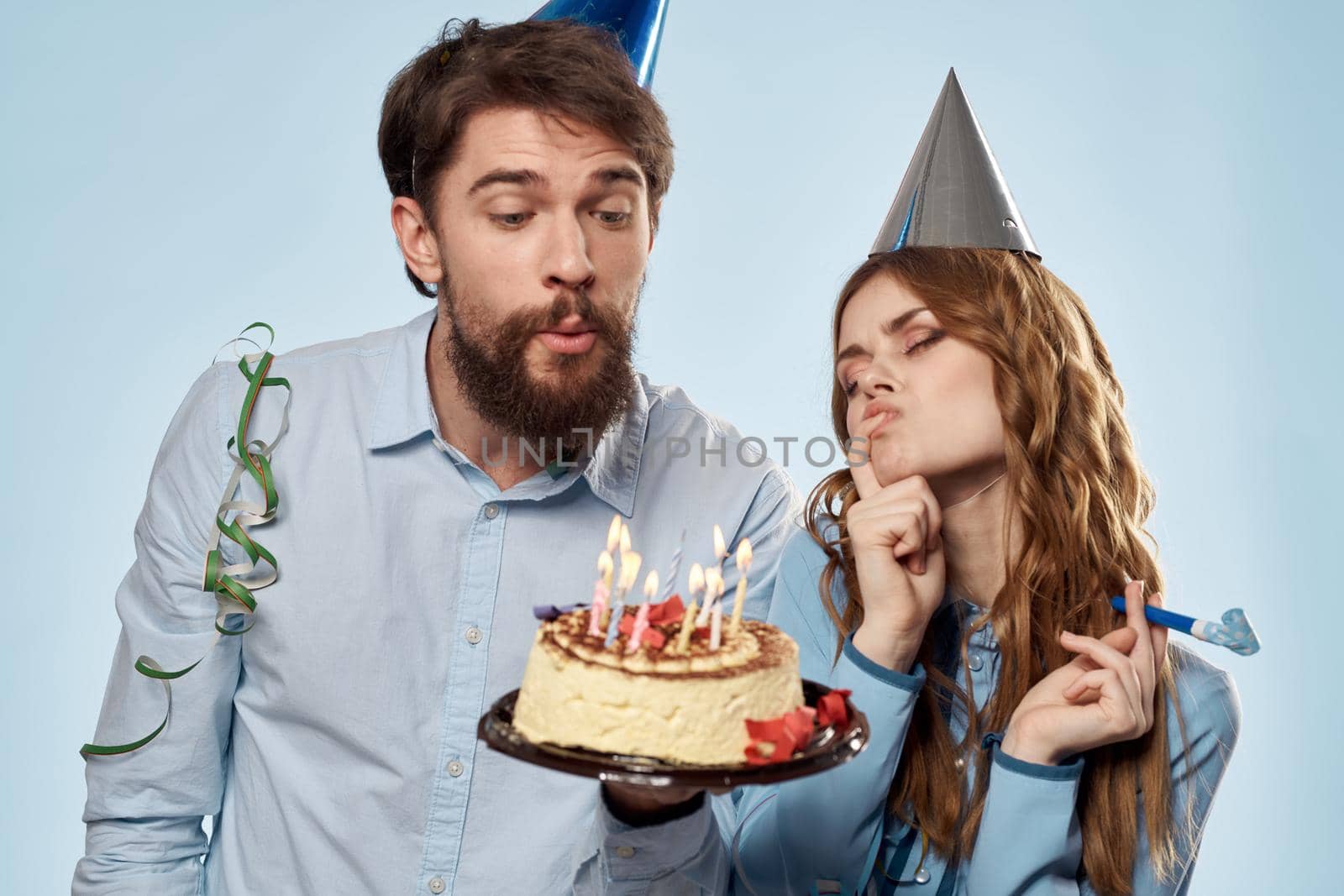 man and woman celebrate birthday with cake and in hats on blue background. High quality photo